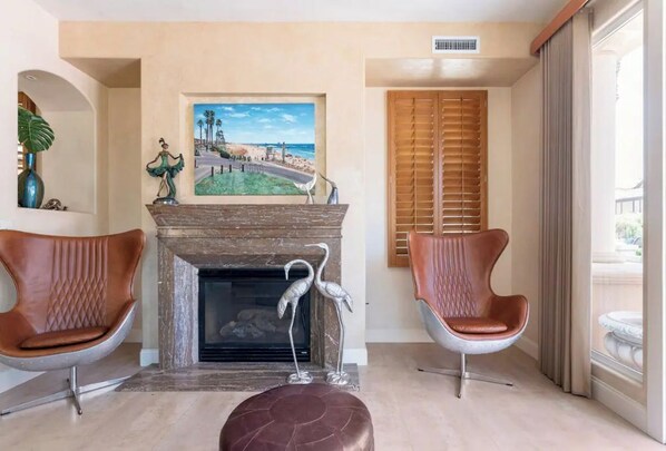 Una sala de estar con chimenea, dos sillones de cuero, una escultura metálica decorativa y un cuadro de una escena costera.