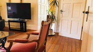 Un salon avec un téléviseur, une table basse en verre, un fauteuil rouge et une plante en pot.