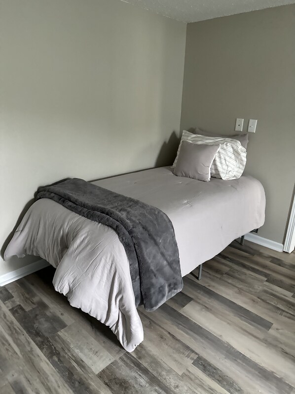 Een slaapkamer met een bed, een grijze deken en een grijs kussen.