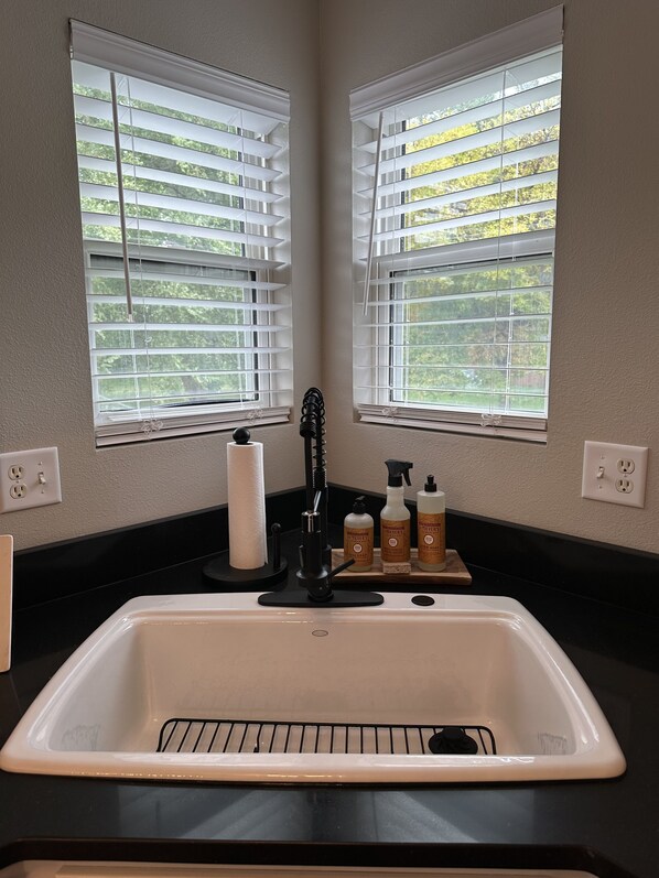 A kitchen with a white sink, two windows with blinds, and toiletries on the counter. - Stellar 4 bedroom home, newly renovated in Ankeny (Ankeny)