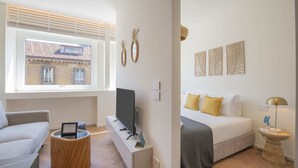 Una habitación de hotel moderna con un gran ventanal, un televisor de pantalla plana, un sofá, una mesita de noche y una cama con almohadas amarillas.