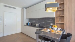 Una cocina moderna con salpicadero de mármol, un comedor con mesa negra y una estantería de madera.