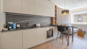 Una cocina moderna con salpicadero de mármol negro, horno integrado y un comedor con una silla y una mesa negros.
