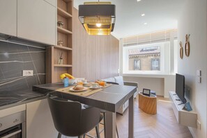 Une cuisine moderne avec un coin repas, un téléviseur et une fenêtre donnant sur des immeubles.