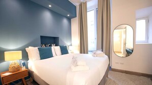 A hotel room with a large bed, a bedside table with a lamp, a welcome sign, a mirror, and a view of the outside.