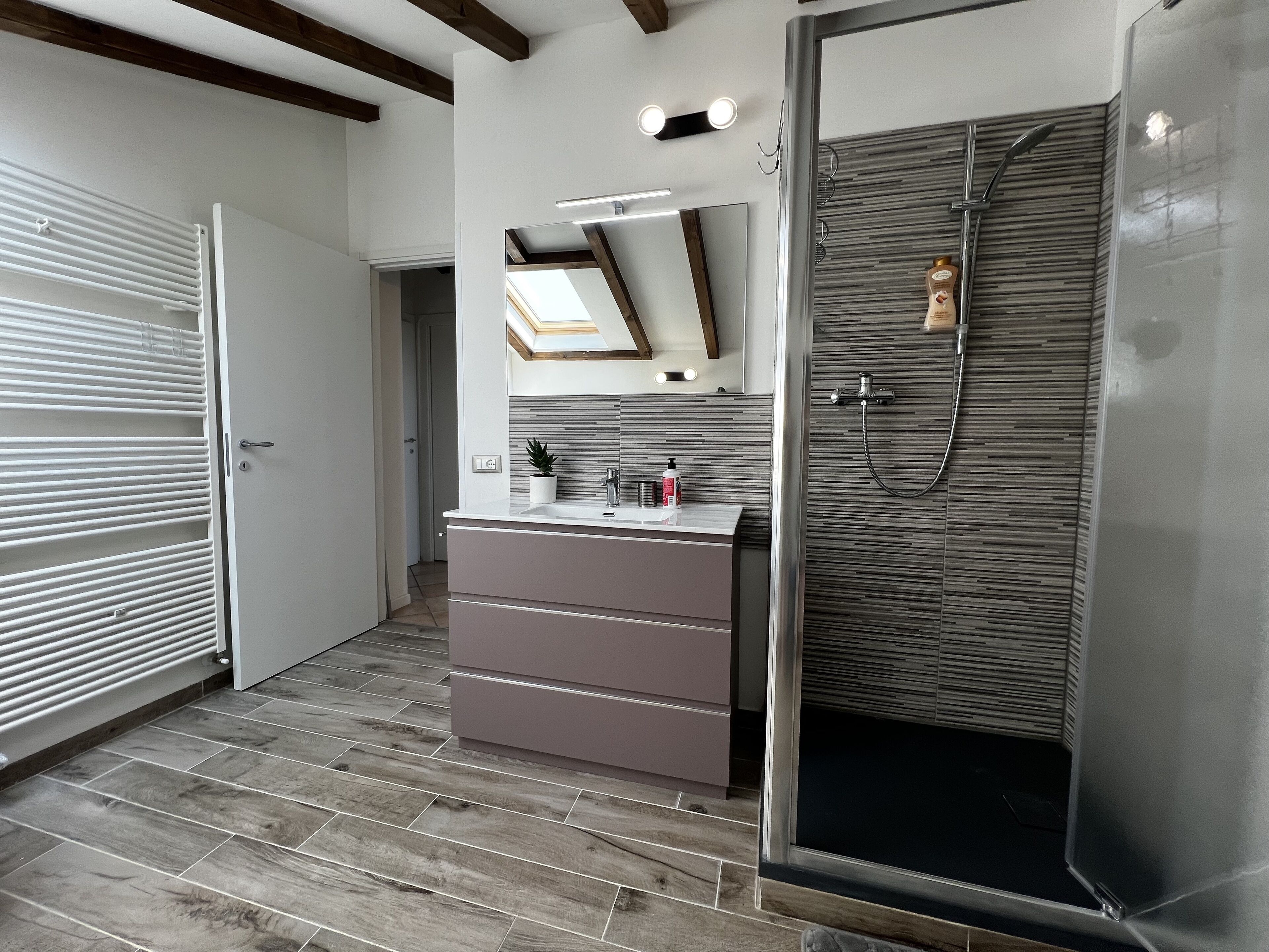 A modern bathroom with a shower, a vanity with a mirror, and a wooden floor.