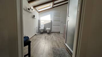 Une petite salle de bain comprenant des toilettes, un bidet et une petite étagère ornée d’objets décoratifs.