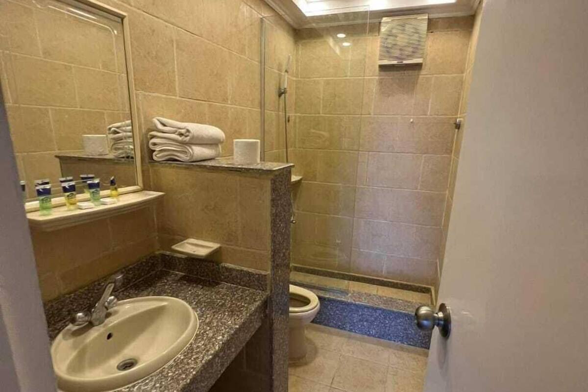 Un baño con lavamanos de encimera de granito, un espejo, cabina de ducha con paredes de vidrio y un inodoro.