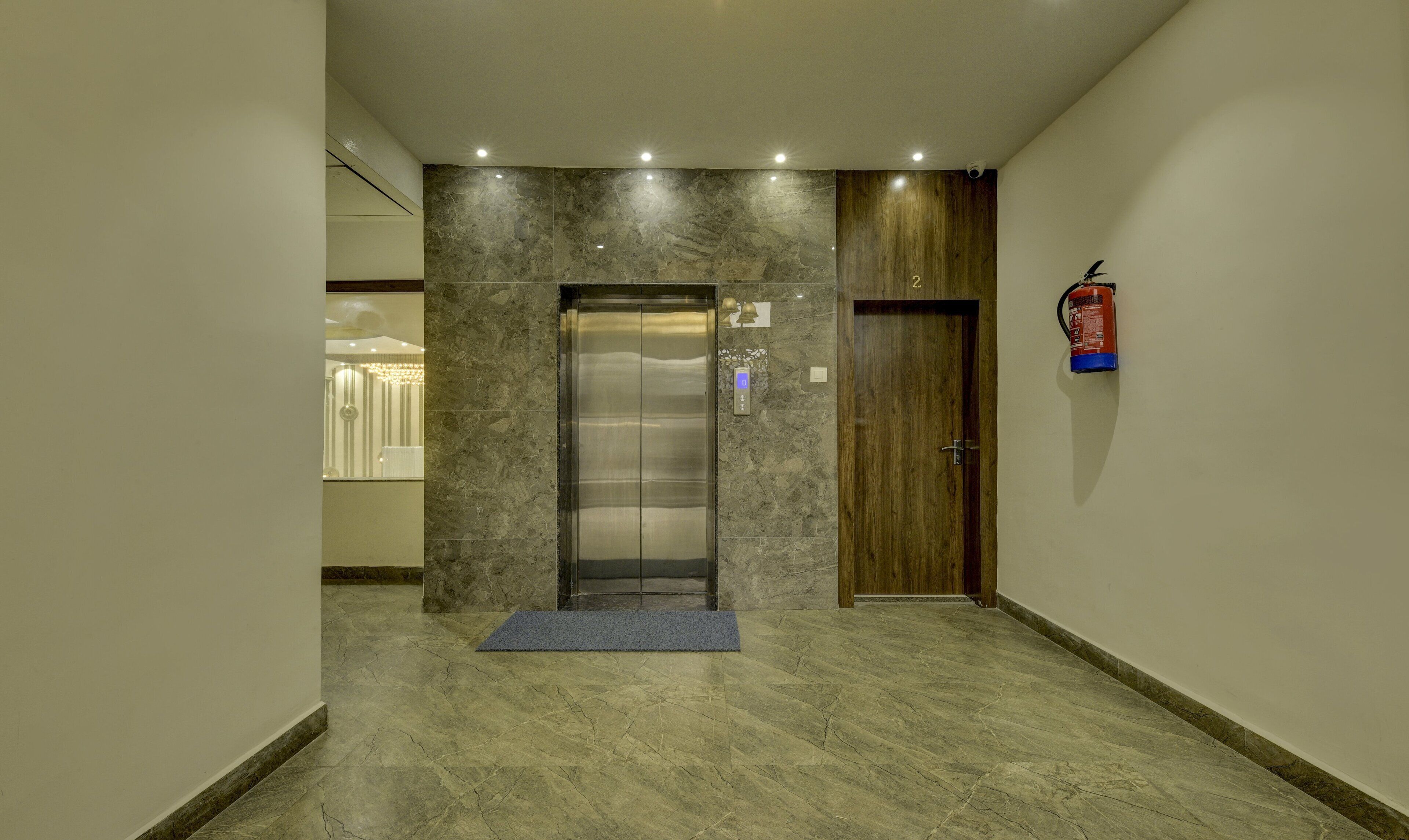 A modern elevator with a digital display, a wooden door, and a fire extinguisher mounted on the wall.