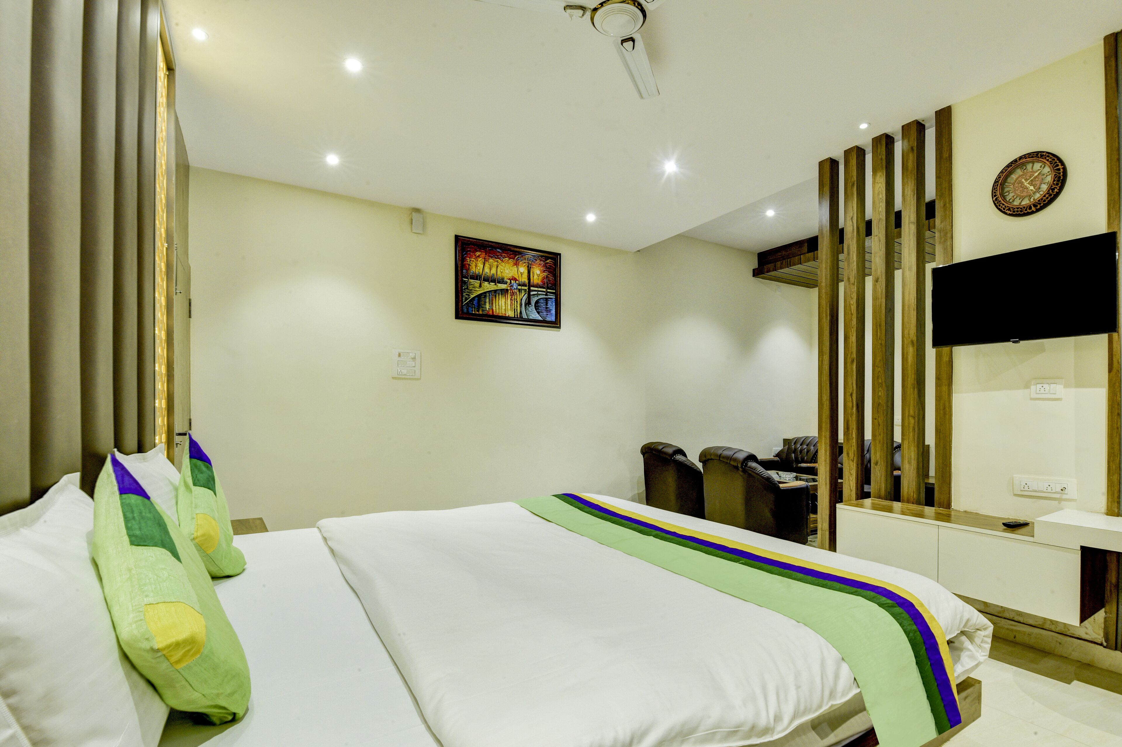 A hotel room with a bed, a painting on the wall, a television, and a wooden panel design.