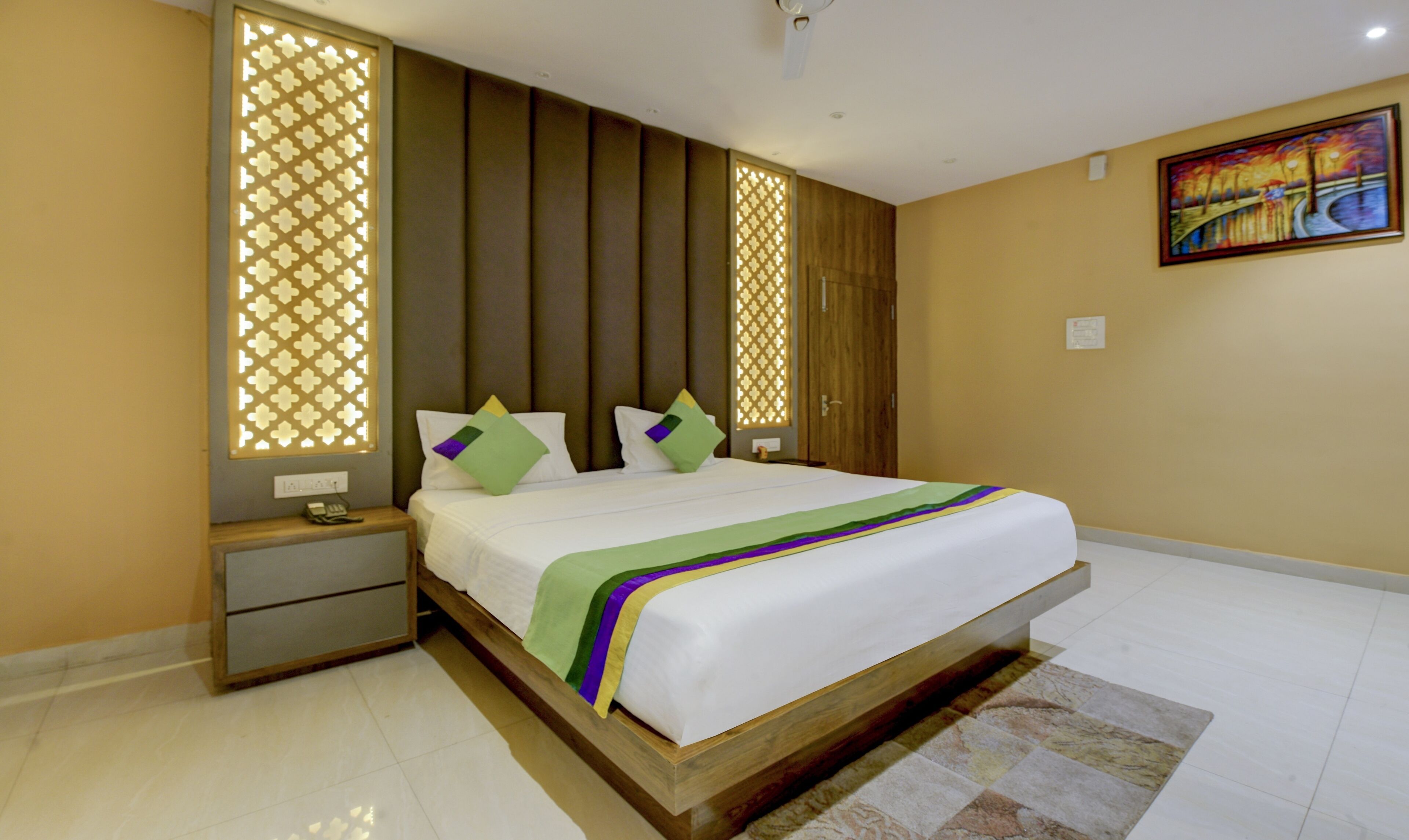 A hotel room with a large bed, a nightstand, a wooden headboard, and a painting on the wall.