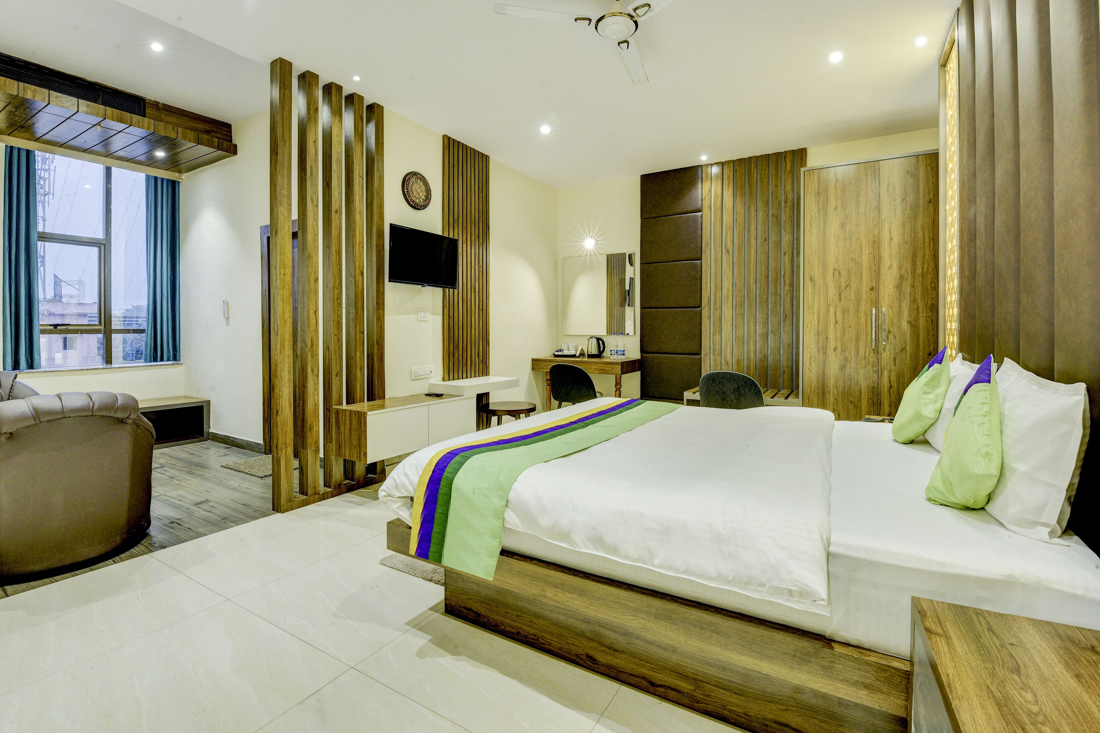 A modern hotel room with a large bed, a desk, a chair, and a wardrobe.