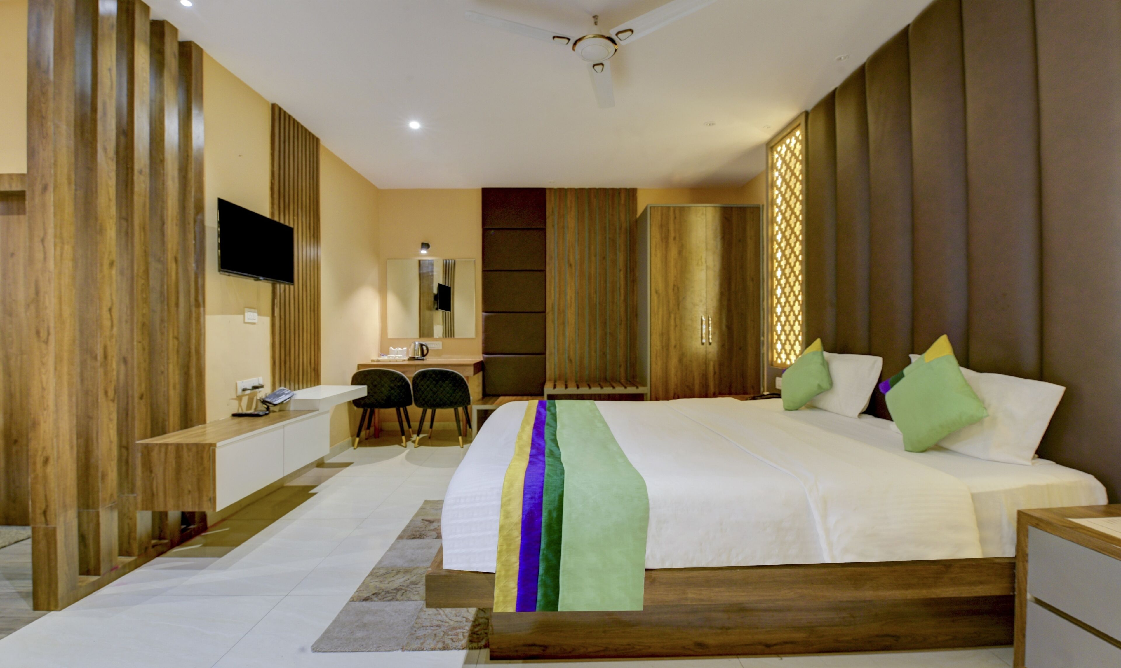 A modern hotel room with a large bed, wooden paneling, a desk, and a television.
