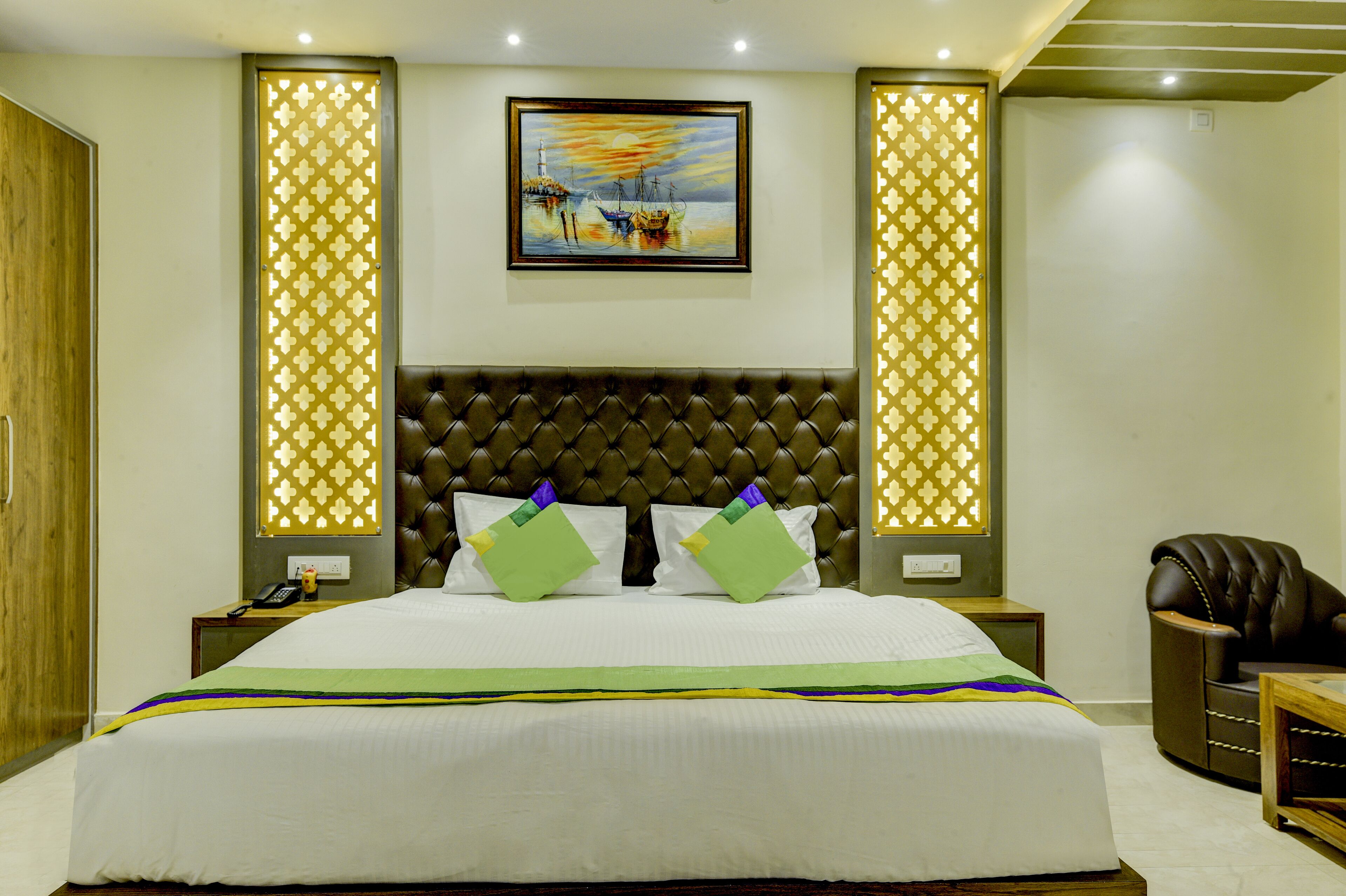 A hotel room with a large bed, a headboard, two nightstands, a leather armchair, and a painting on the wall.