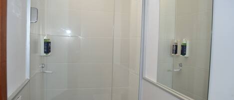 Un baño con cabina de ducha de vidrio, un espejo y artículos de aseo en la pared.