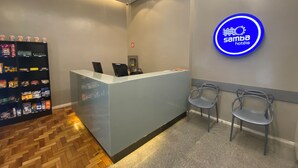 A reception desk with a blue neon sign, two chairs, a vending machine, and a wooden floor. - Samba Belo Horizonte Vintage (Belo Horizonte)