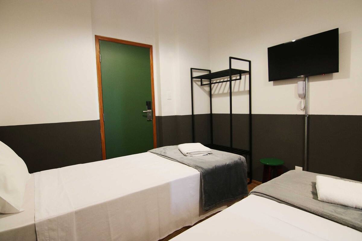 A hotel room with two beds, a TV mounted on the wall, and a green door.