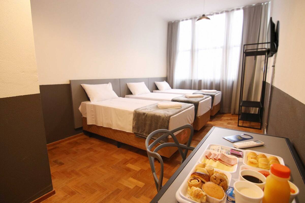 A hotel room with two beds, a dining table with breakfast items, a TV, and a window with curtains.