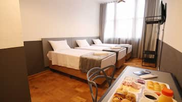 Habitación de hotel con dos camas, una mesa de comedor con alimentos para el desayuno, un televisor y una ventana con cortinas.
