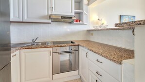 A kitchen with white cabinets, a stainless steel oven, a granite countertop, and a built-in microwave. - Caribbean Court - Harbor View Apartment (Kralendijk)