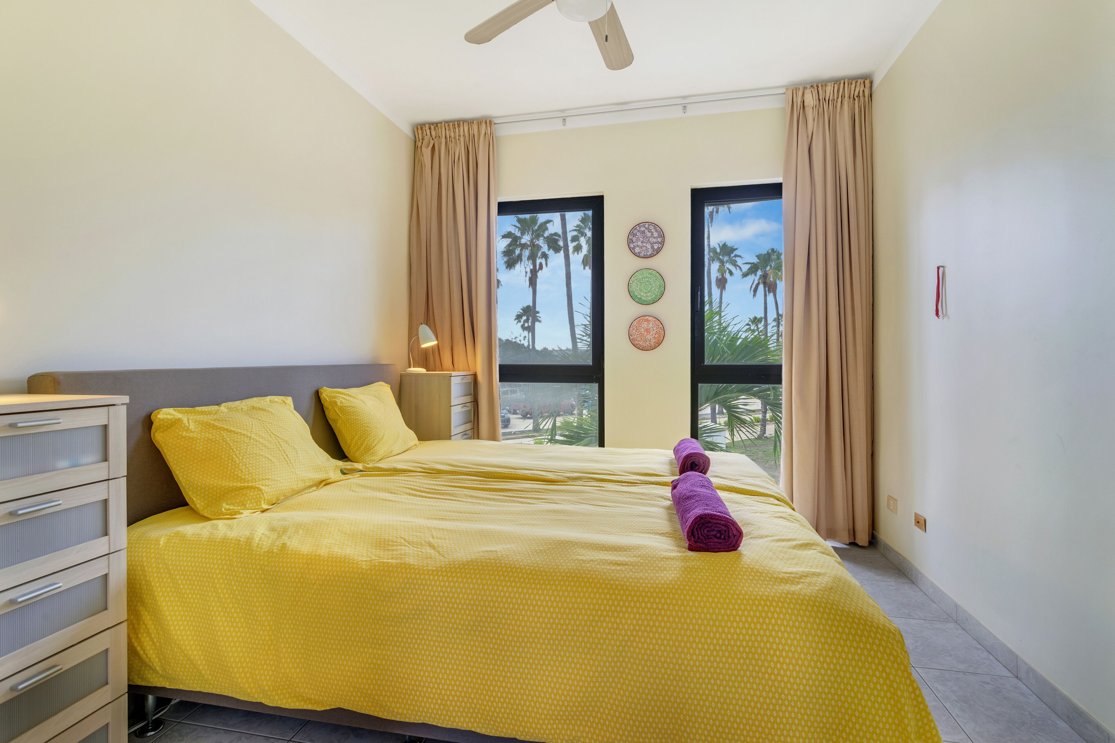 Una habitación de hotel con cama, cómoda, mesita de noche y ventana con cortinas.