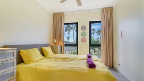 A hotel room with a bed, a dresser, a nightstand, and a window with curtains. - Caribbean Court - Harbor View Apartment (Kralendijk)