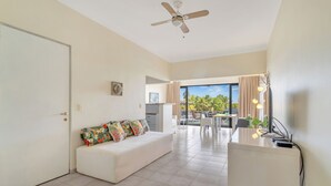 A modern living room with a white sofa, a ceiling fan, and a view of the outdoors. - Caribbean Court - Harbor View Apartment (Kralendijk)