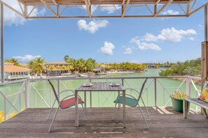 A wooden deck with a table and chairs overlooking a body of water, surrounded by palm trees and buildings. - Caribbean Court - Harbor View Apartment (Kralendijk)