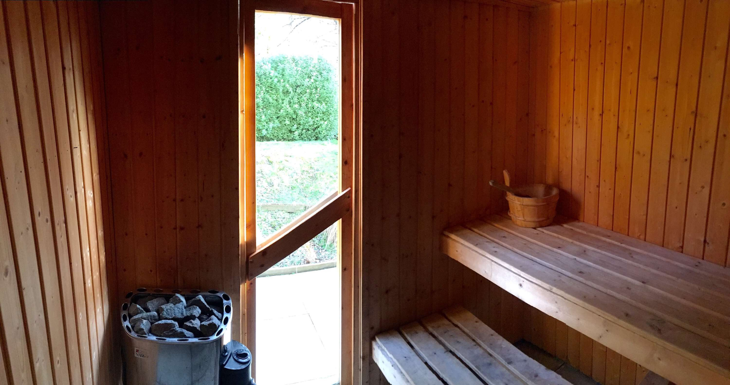 A sauna room with wooden walls, a bench, a small wooden shelf, and a window.