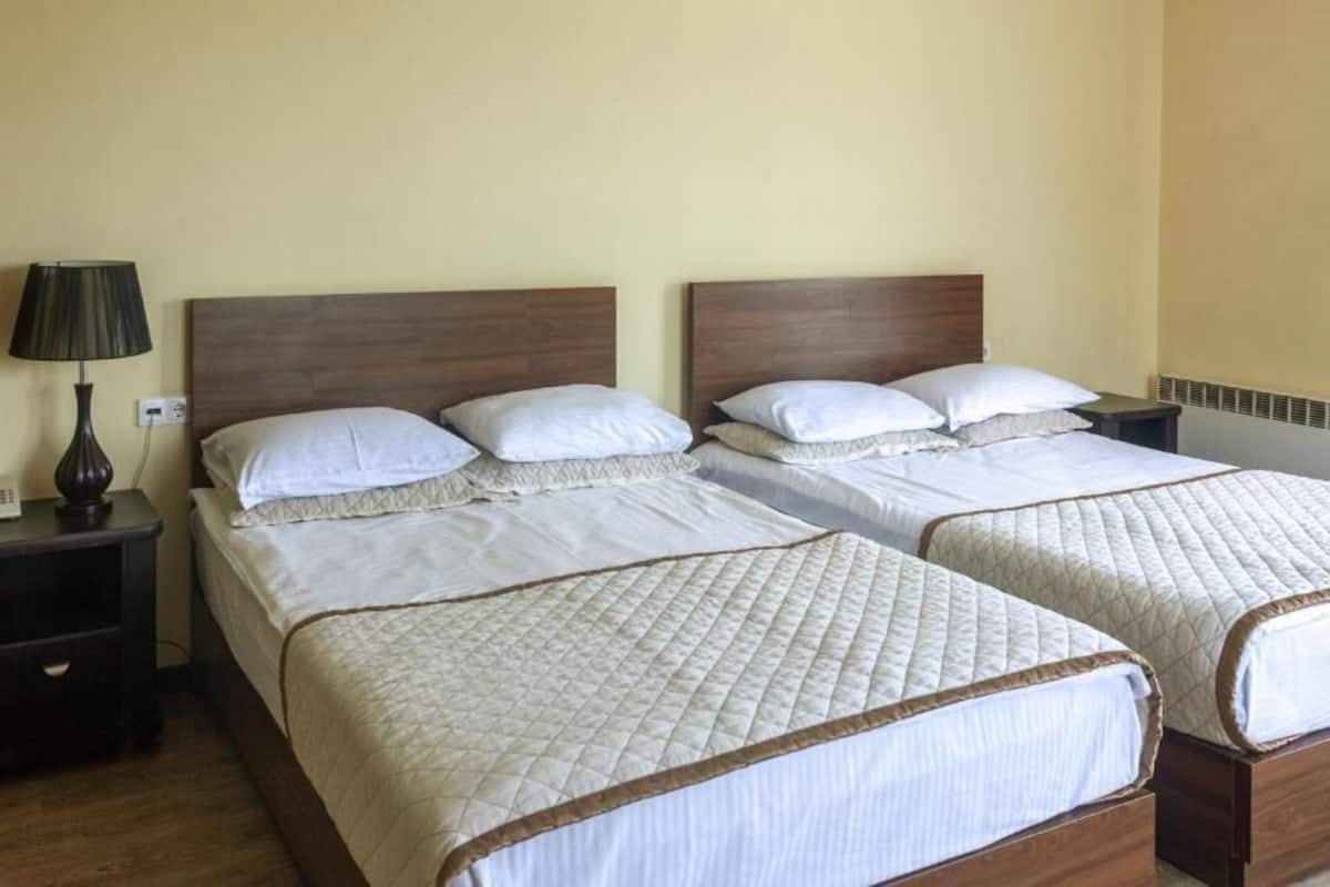 Ein Hotelzimmer mit zwei Betten, beide mit weißer Bettwäsche und einer gesteppten Daunendecke. Ein Nachttisch mit Lampe befindet sich auf der linken Seite.