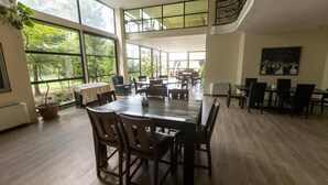 A spacious dining area with large windows, wooden tables, and chairs. - Hotel Beaumonde Garden (Tbilisi)