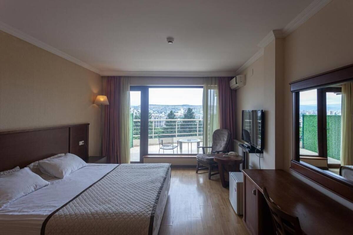 Ein Hotelzimmer mit Bett, Schreibtisch, Sessel, Fernseher und einem Balkon mit Aussicht.