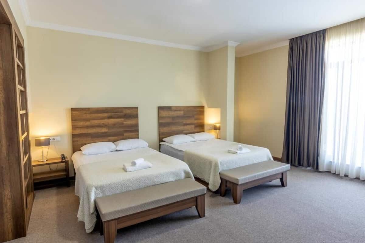 Ein Hotelzimmer mit zwei Betten, einer Bank und einem Nachttisch mit einer Lampe.