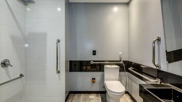 A modern bathroom with a shower, toilet, and sink, featuring grab bars and a black countertop.