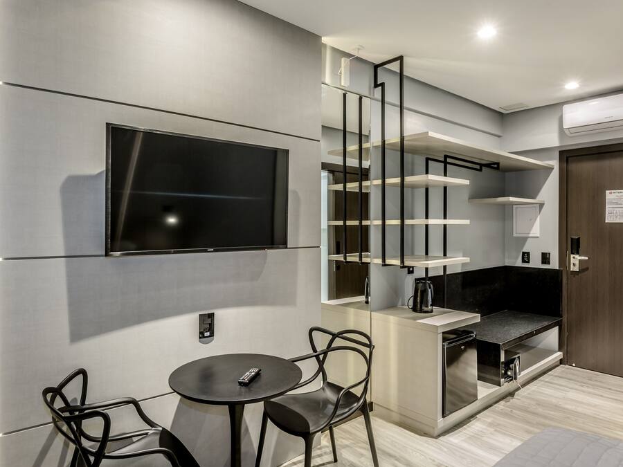 A modern kitchen with a built-in TV, a dining area with two chairs, and a staircase with open shelving.