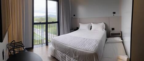 A hotel room with a large bed, a desk, and a view of the outdoors.