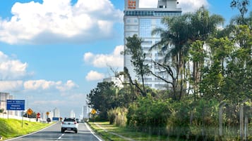 A road with a white car, a hotel with a 'tri' sign, and greenery on the side.