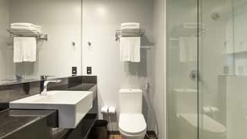 Un baño moderno con un espejo grande, un lavamanos blanco, un inodoro y una ducha con mampara de vidrio.
