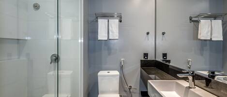 Un baño moderno con ducha envuelta en vidrio, inodoro blanco, tocador con lavamanos y dos barras para toallas.