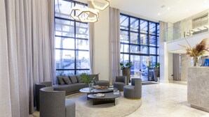 A spacious living area with a large sofa, a coffee table, and two armchairs. There are large windows with curtains, a chandelier, and a plant on a marble table. - Tri Hotel Premium Itapema (Itapema)