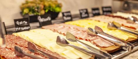 Un bufé con varias carnes y quesos, incluyendo jamón, salami y diferentes tipos de queso, dispuestas sobre tablas de madera.