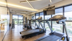A modern gym with treadmills, weights, and a large window offering a view of the outdoors. - Tri Hotel Premium Itapema (Itapema)