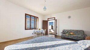 A bedroom with a bed, a sofa, a dining table with chairs, and a view of the sea through a window. - 2142 Villetta Roberta - Primo Piano by Barbarhouse (Nardò)