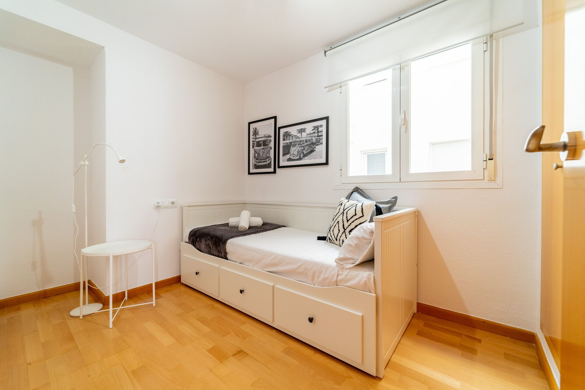 A bedroom with a bed, a bedside table, a lamp, and two framed pictures on the wall.