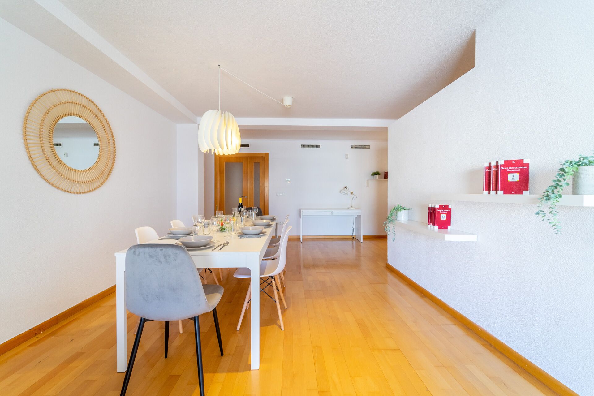 A modern dining area with a white table, grey chairs, and a hanging light fixture.