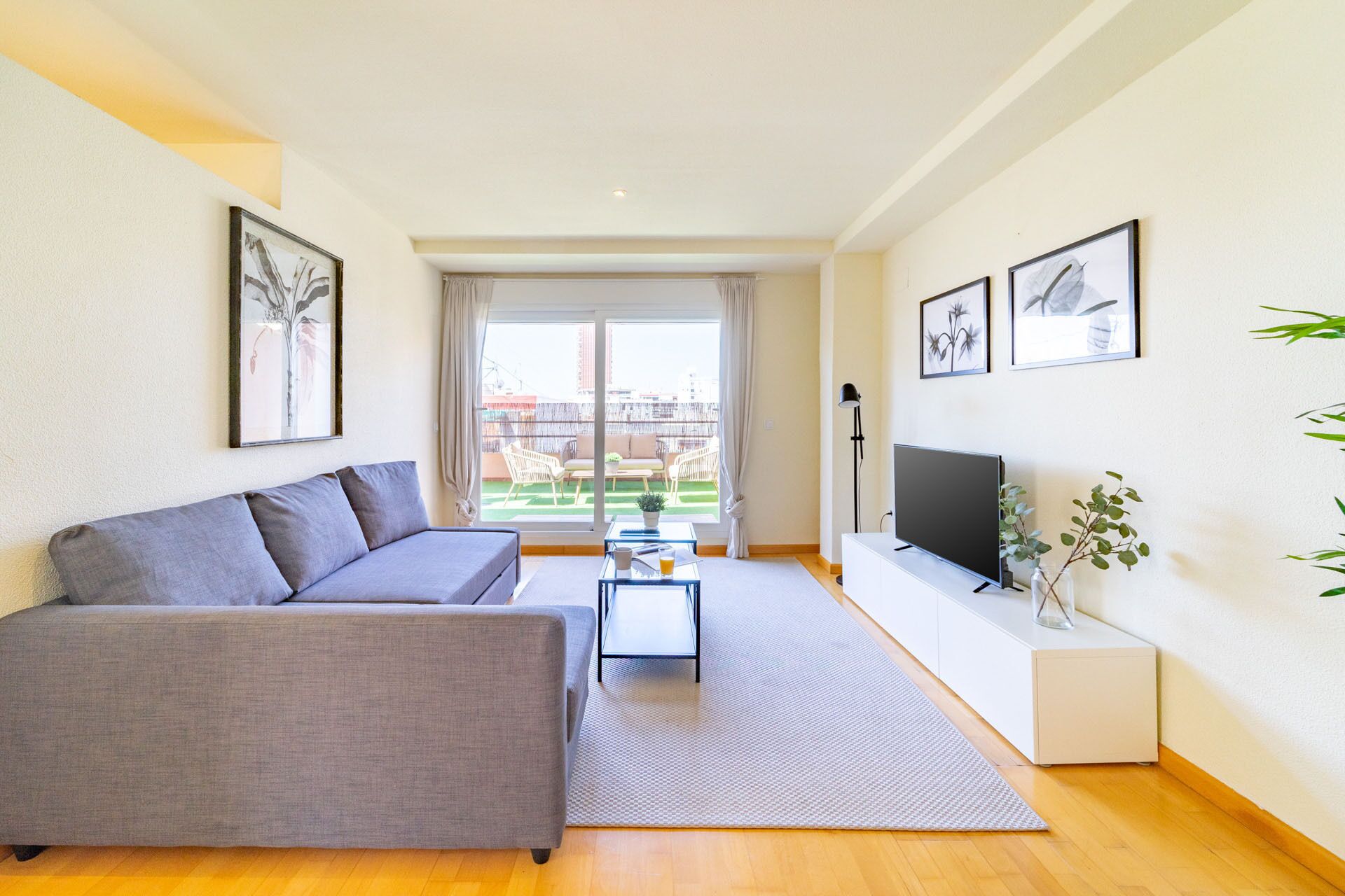 Een moderne woonkamer met een grijze bank, een flatscreen televisie en een klein bijzettafeltje.