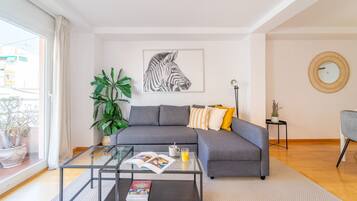A modern living room with a grey sofa, a glass coffee table, a large potted plant, and a framed zebra artwork on the wall.