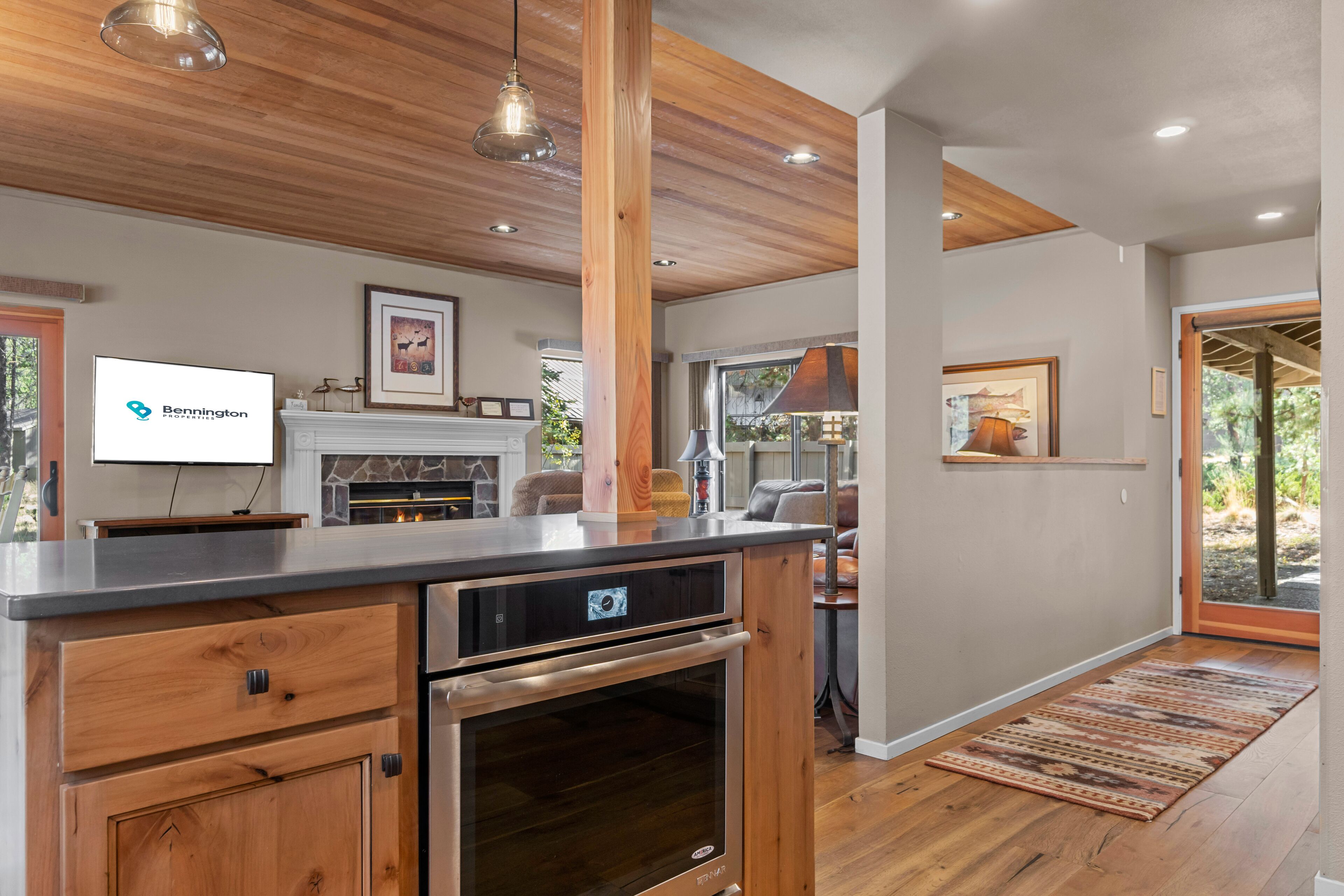 A modern kitchen with a stone fireplace, wooden cabinetry, and a built-in oven.