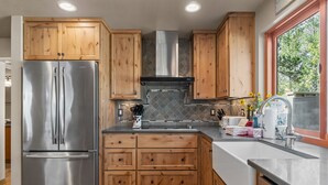 Una cocina con armarios de madera, un refrigerador de acero inoxidable, una estufa a gas y una ventana con vista a árboles.