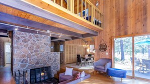 A cozy living room with a stone fireplace, wooden floors, and a balcony with wooden railings. - DESC09 - Retro Home, Sunken Living Room, Private Hot Tub (Sunriver)